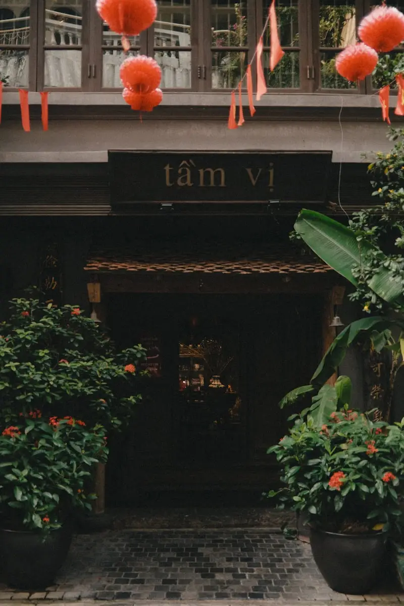 (2026) A Table At: Tแบงm Vแป, Hanoi The wooden facade of Tแบงm Vแป restaurant in Hanoi, framed by greenery