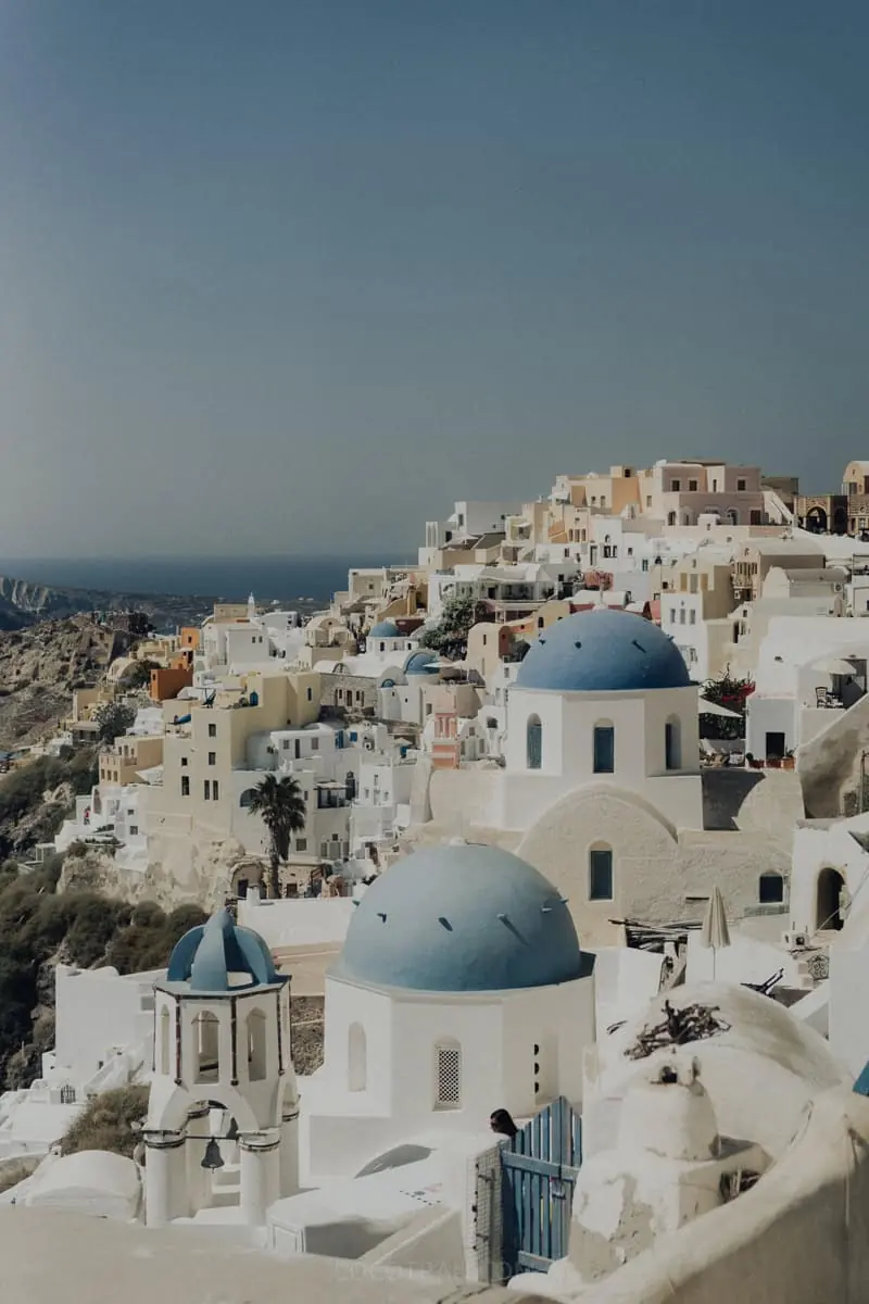 Blue-domed churches and white cave houses stacked down the cliff in Oia, Santorini